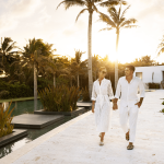 A couple dressed in white strolling through the serene surroundings of Ceiba Club at Conrad Tulum.