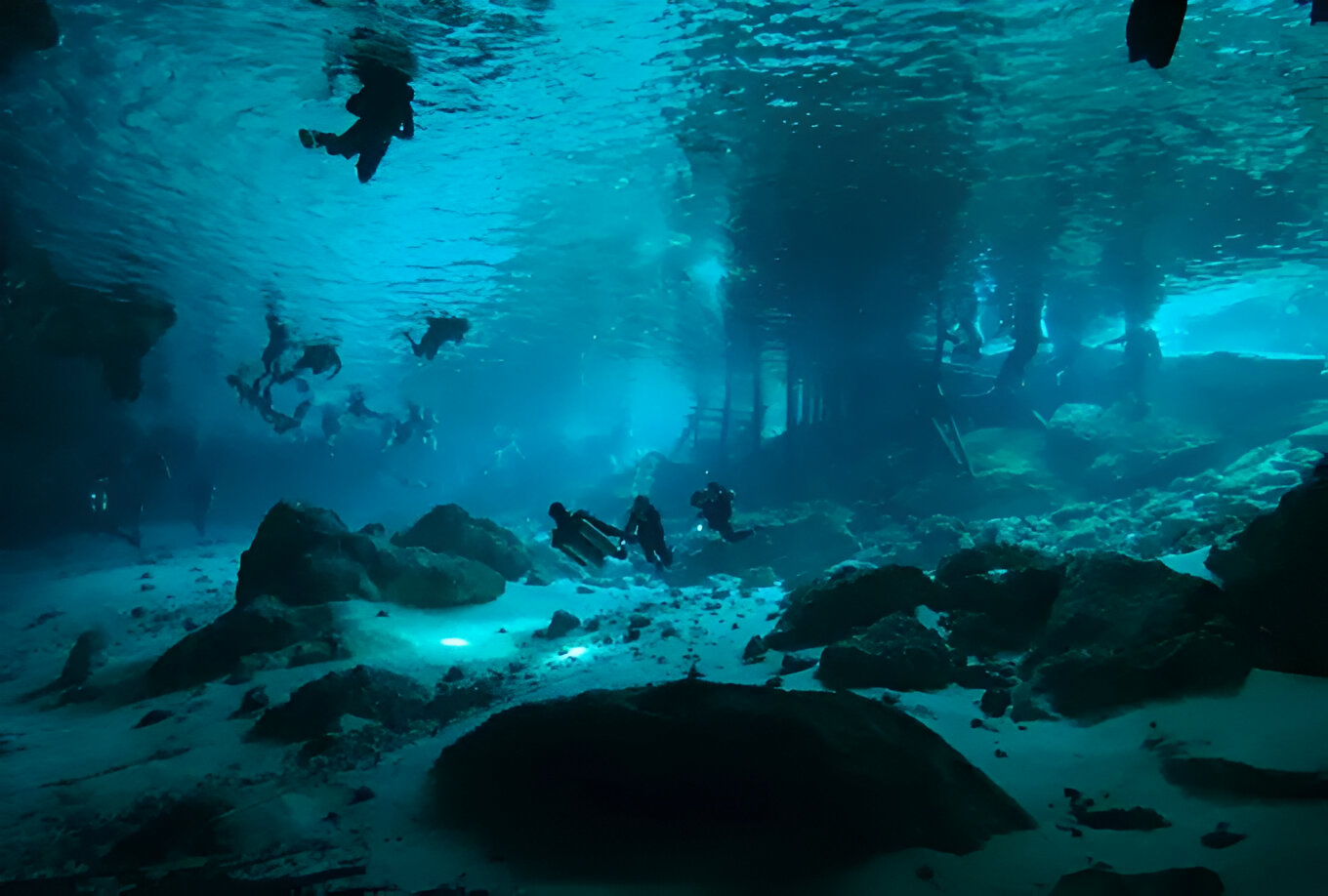 People diving in a cenote in Tulum, surrounded by clear water and natural rock formations