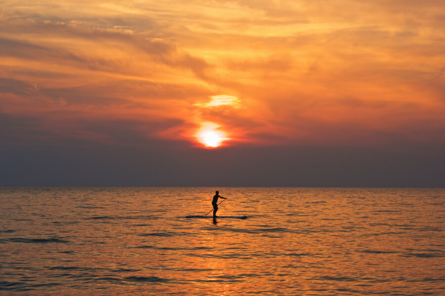 Person paddleboarding at sunset, enjoying the tranquil waters and vibrant sky