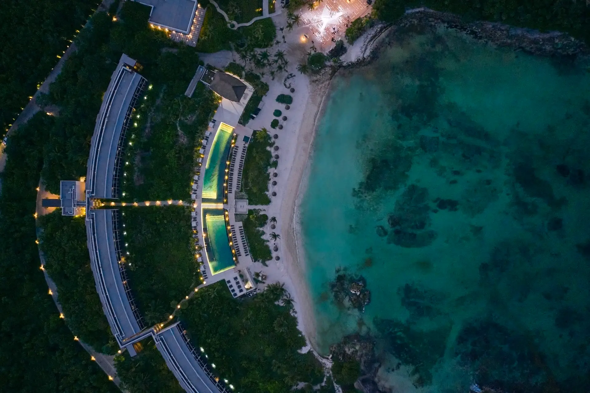 Aerial view of Conrad Tulum at dusk, highlighting the resort's illuminated features against the backdrop of a colorful sunset