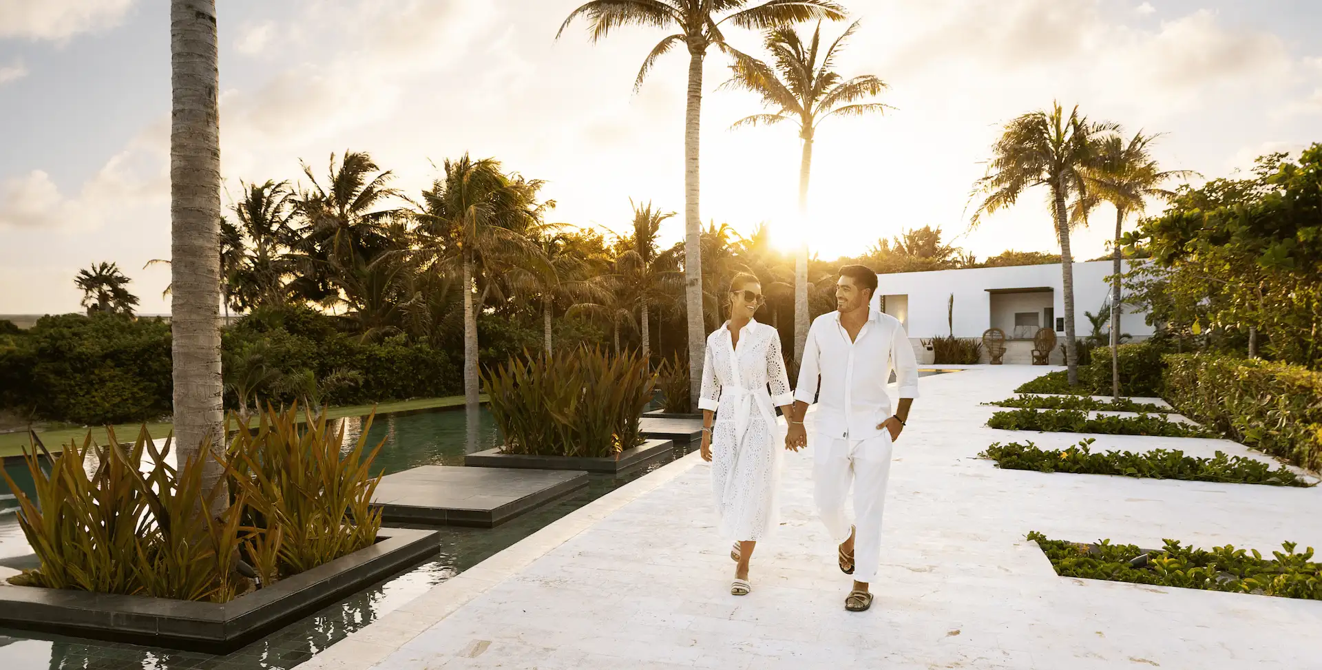 A couple dressed in white strolling through the serene surroundings of Ceiba Club at Conrad Tulum.