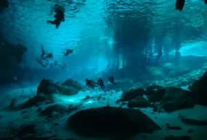 Cenote in Tulum with people diving in crystal-clear water surrounded by natural rock formations